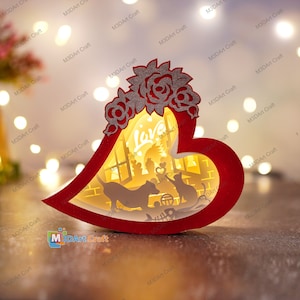 May include: A red heart-shaped wooden light-up box with a cut-out design of a house, a dog, a cat, and the word "Love". The box is decorated with a silver floral design.