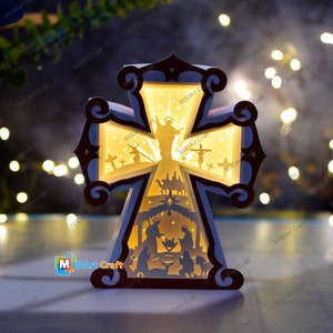 Puede incluir: Una cruz de madera con una luz en su interior, que representa la escena de la natividad y los tres reyes magos. La cruz está iluminada con un brillo cálido, creando un ambiente festivo.