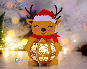 Op de afbeelding: Een gouden rendierfiguur met een rode kerstmanmuts en sjaal houdt een lantaarn vast met een gloeiend licht erin. Het rendier heeft een vrolijke uitdrukking en staat op een houten oppervlak.