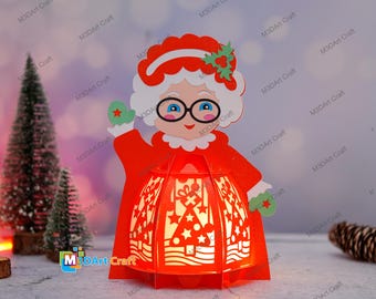 May include: Red and white Christmas lantern shaped like a woman wearing a red dress and a white hat with holly. The lantern has a white cutout design of a Christmas tree and stars.