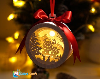 May include: A white papercraft ornament with a red ribbon. The ornament features a cut-out design of Santa Claus with a gift bag, a snowy mountain scene, and a small rabbit. The ornament is illuminated from behind, creating a warm glow.
