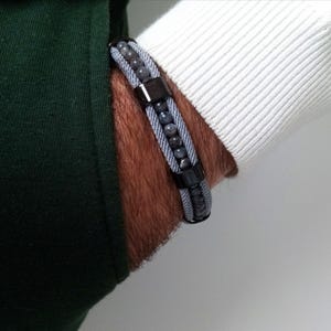 Peut inclure: Un bracelet gris et noir perlé avec des accents métalliques. Le bracelet est composé de deux brins de cordon gris avec des perles noires et des accents métalliques.