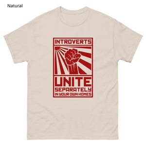 May include: A natural-colored t-shirt with a red graphic. The graphic features the word "INTROVERTS" above a clenched fist, rays, and the word "UNITE" with the phrase "SEPARATELY IN YOUR OWN HOMES" below.