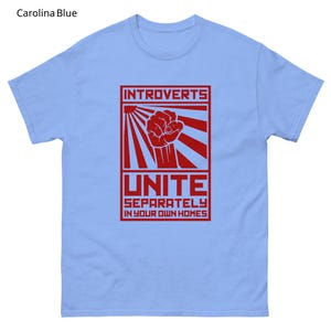 May include: Carolina blue t-shirt with a red graphic. The graphic features the word "INTROVERTS" above a clenched fist and the word "UNITE" with the phrase "SEPARATELY IN YOUR OWN HOMES" below.