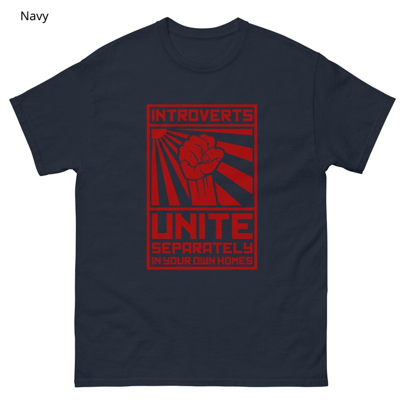 May include: Navy blue t-shirt with a red graphic. The graphic features the text "Introverts Unite Separately in Your Own Homes" with a fist and sunburst design. The shirt is made of a soft material.