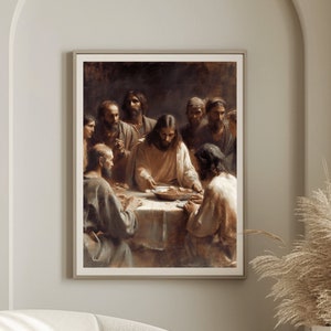 May include: A beige armchair with a white throw blanket sits in front of a painting depicting a group of people gathered around a table. The painting is framed in a simple black frame and hangs on a light beige wall. A tall vase with dried pampas grass sits on a wooden table next to the armchair.