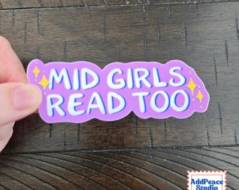 May include: A purple die-cut sticker with a wavy border featuring the white text "MID GIRLS READ TOO" in a bold, rounded font. The design includes small yellow four-pointed star accents on the left and right sides of the text.