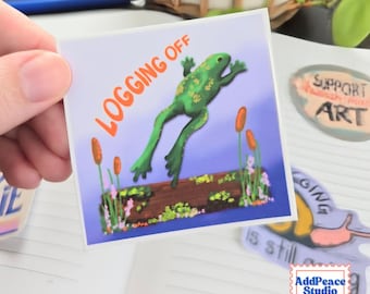 May include: A square sticker featuring a green frog leaping away from a brown log in a pond. The text LOGGING OFF is printed in orange letters in the upper left corner. The scene includes cattails and small pink flowers against a purple background.