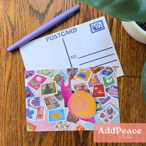 May include: A postcard featuring a collage of stamps and a pink snail illustration. A purple pen and a blank postcard with the word "POSTCARD" are visible. The postcard rests on a wooden surface.
