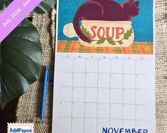 May include: A spiral-bound calendar featuring a whimsical illustration of a black cat in a soup bowl. The word "SOUP" is displayed on the bowl. The calendar shows the month of November. The calendar's dates span from July 2026 to June 2027.