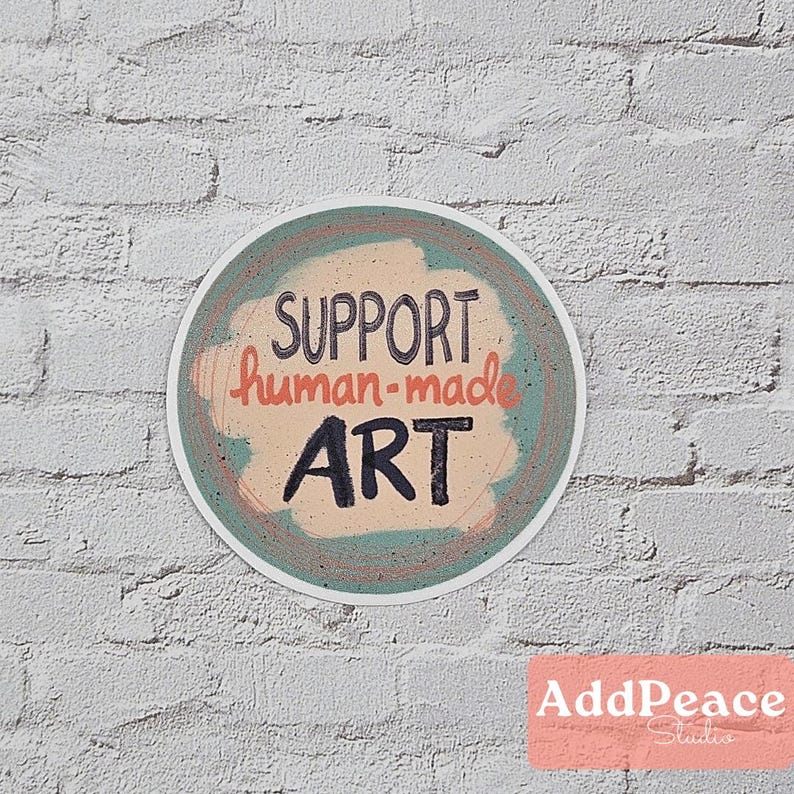 May include: A round sticker with a teal and peach background. The sticker has the text "SUPPORT human-made ART" in black and orange lettering.