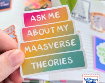 May include: A rectangular sticker with rounded corners featuring a vibrant rainbow gradient background. The text is printed in white, bold, sans-serif capital letters, reading: ASK ME ABOUT MY MAASVERSE THEORIES, arranged in four distinct horizontal lines.