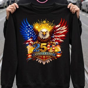 May include: Black sweatshirt with a patriotic eagle design. The eagle has wings in the style of the American flag, with the text "250 Anniversary 1776-2026". The design features red, white, and blue colors, and is centered on the front of the garment.