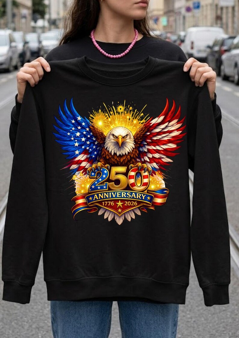 May include: Black sweatshirt with a patriotic eagle design. The eagle has wings in the style of the American flag, with the text "250 Anniversary 1776-2026". The design features red, white, and blue colors, and is centered on the front of the garment.