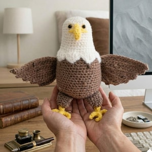 May include: A handmade crochet eagle with a white head, brown body and wings, and yellow feet. The eagle is held in open hands. The craft project is a decorative item.