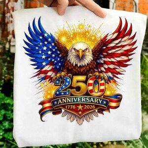 May include: White tote bag with a patriotic design. It features an eagle with wings in red, white, and blue, resembling the American flag. The text reads "250 Anniversary 1776-2026".