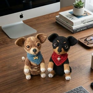 Puede incluir: Dos figuras de perro Chihuahua hechas a mano con ganchillo. Una es marr&oacute;n y canela con un pa&ntilde;uelo azul y un dije de hueso, la otra es negra y canela con un pa&ntilde;uelo rojo y un dije de coraz&oacute;n. Est&aacute;n sobre un escritorio de madera.