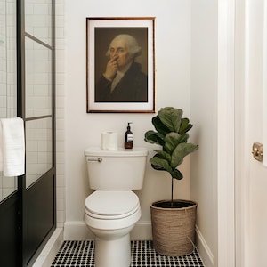 May include: A bathroom scene featuring a white toilet, a framed portrait of George Washington, and a potted plant in a woven basket. The floor has a black and white tile pattern. A roll of toilet paper and a soap dispenser sit on the toilet tank.
