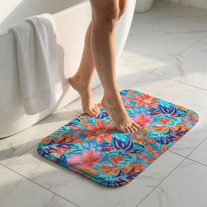 May include: A rectangular bath mat featuring a vibrant, multi-colored floral pattern on a bright blue background. The design includes stylized flowers and leaves in shades of pink, orange, red, and dark blue, with rounded corners and a soft texture.