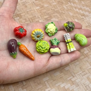 May include: A collection of ten miniature ceramic vegetable figurines including a red tomato, orange carrot, purple eggplant, yellow pumpkin, green cauliflower, lettuce, turnip, asparagus bundle, broccoli, and a light green bean.