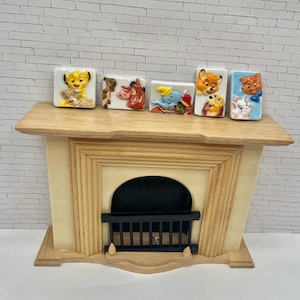 May include: A miniature fireplace mantel made of wood, with a light beige finish. Six rectangular ceramic figurines with Disney character designs are displayed on the mantel. The figurines feature characters from The Lion King, Dumbo, and other Disney films.