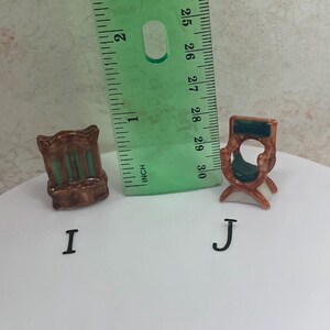 May include: Two miniature ceramic chairs, one with a brown frame and green accents, the other with a brown frame and a green seat. A green ruler is placed next to the chairs. The chairs are labeled with the letters "I" and "J".