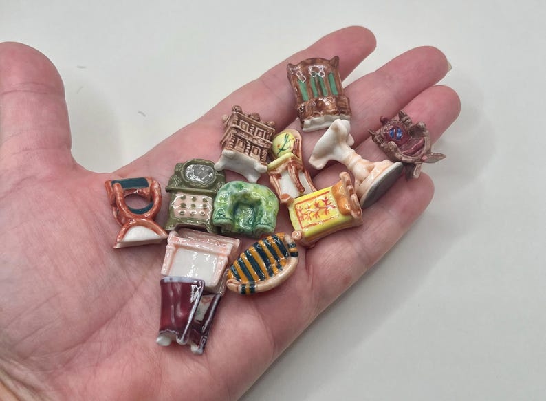 May include: A collection of miniature ceramic furniture pieces, including chairs, a clock, and a table, in various colors and designs. The pieces are held in a hand, showcasing their small size and intricate details. The collection includes a variety of styles.