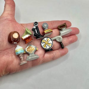 May include: A collection of miniature ceramic figurines, including a radio, gramophone, telephone, microphone, iron, hairdryer, fan, and lamps. The figurines are painted in various colors and styles, showcasing vintage and retro designs.