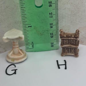 May include: Miniature ceramic furniture set including a pedestal table and a cabinet. The table is approximately 1 inch tall, and the cabinet is about 1.25 inches tall. Both pieces are painted in shades of beige and brown.