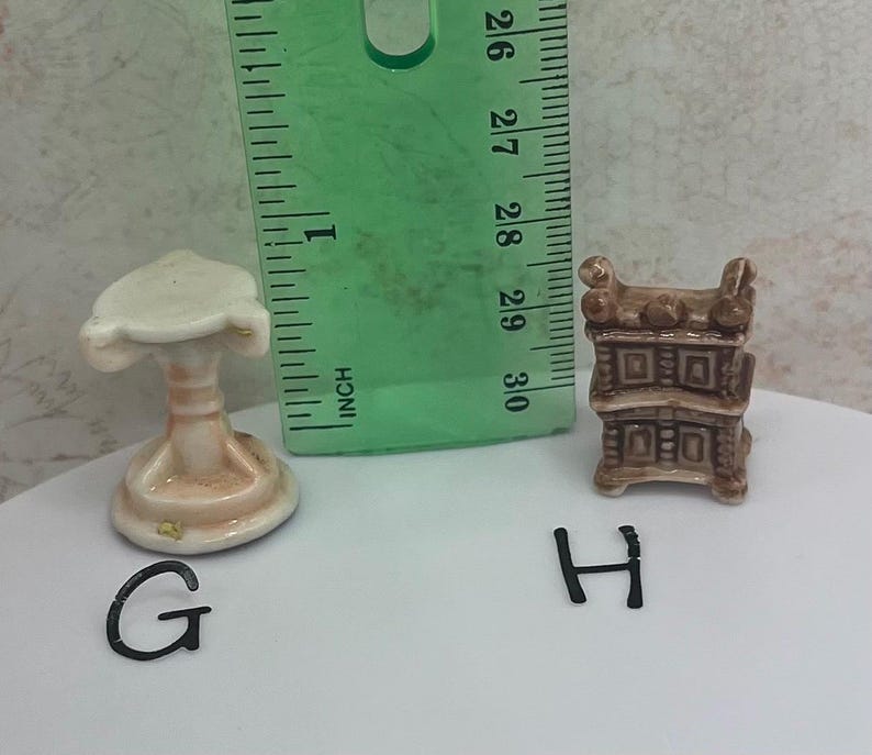 May include: Miniature ceramic furniture set including a pedestal table and a cabinet. The table is approximately 1 inch tall, and the cabinet is about 1.25 inches tall. Both pieces are painted in shades of beige and brown.