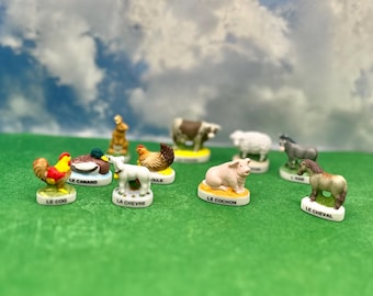 May include: A collection of miniature ceramic farm animal figurines, including a rooster, duck, goat, pig, and horse. Each figurine is on a small base with a French word. The figurines are set on a green surface.