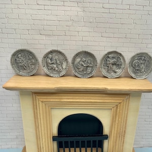 May include: Five gray decorative plates with relief scenes of people in historical settings. The plates are round with a textured border and are displayed on a wooden mantelpiece. The scenes depict various activities.