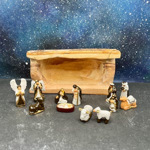 May include: A ceramic nativity scene with figures of angels, the holy family, and animals. The figures are painted with gold accents and set in front of a wooden manger. The background is a starry night sky.