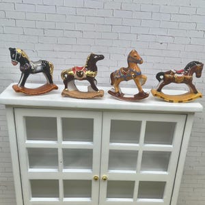 May include: Four miniature ceramic rocking horse figurines displayed in a row. Each horse features a unique color scheme including black, dark brown, tan, and light brown, with painted saddles, bridles, and gold-toned accents on their curved rockers.