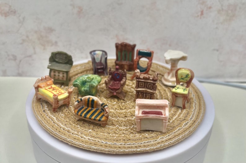May include: A collection of miniature furniture pieces, including chairs, a bed, a sofa, and a piano. The furniture is painted in various colors and styles, arranged on a round, woven surface.