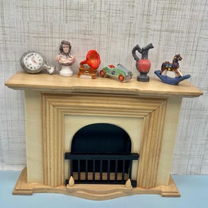 May include: A miniature fireplace mantel with decorative items. The mantel is light wood with a cream-colored front. Items include a clock, bust, gramophone, car, vase, and rocking horse. The items are small and colorful, adding a touch of whimsy.