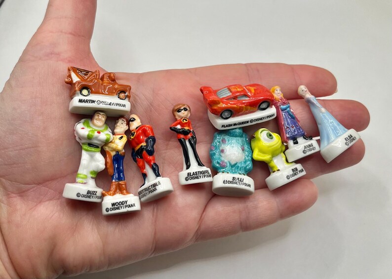 May include: A collection of small, colorful Disney and Pixar character figurines, including Buzz Lightyear, Woody, and characters from The Incredibles and Cars. Each figurine is mounted on a white base with the character's name.