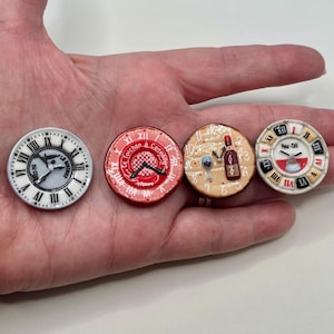 May include: Four small, round decorative clock faces with Roman numerals. The first is white with black details, the second is red with white text, the third is tan with a wine theme, and the fourth is white with red and black details.