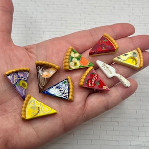 May include: A collection of miniature pie slice charms with various fruit and chocolate designs. Each slice has a golden crust and colorful toppings, including plums, strawberries, and cherries. A small white pie server is also included.