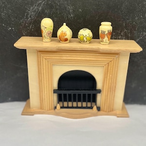May include: A miniature wooden fireplace mantel with a black grate and four small cream-colored ceramic vessels on top. The vessels feature hand-painted illustrations of birds, a tiger, frogs, and owls in orange, green, and brown tones.