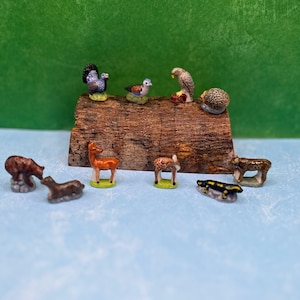 May include: A collection of miniature ceramic animal figurines, including a bear, deer, and bird, displayed on a small wooden platform. The figurines are painted with detailed features and vibrant colors, showcasing a variety of wildlife.