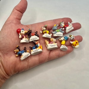 May include: A collection of small, colorful figurines of cartoon dogs, each with unique outfits and accessories. The figurines are white with various colors, including red, blue, yellow, and brown. Each figurine has the text "Pat'Patrouille" on the base.