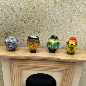 May include: Four miniature ceramic vases with colorful designs. The vases are displayed on a wooden shelf. The first vase is blue with floral accents, the second is yellow and brown, the third is green and yellow, and the fourth is yellow and orange.