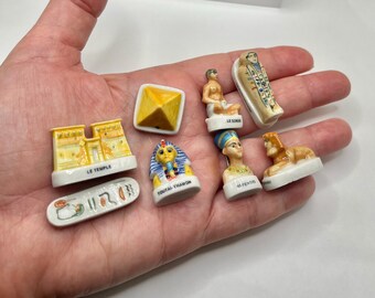 May include: A collection of miniature ceramic Egyptian figurines, including a pyramid, pharaoh busts, a sarcophagus, and a sphinx. The figurines are painted with bright colors and detailed designs, showcasing ancient Egyptian art.