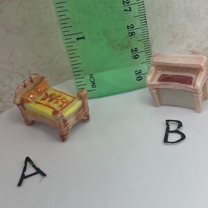 May include: Miniature ceramic furniture set including a bed and a piano. The bed has a yellow mattress with a red and yellow design, and the piano has a red interior. The bed measures approximately 1 inch in length.