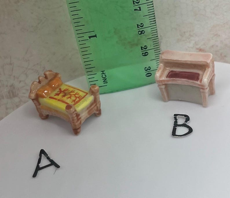 May include: Miniature ceramic furniture set including a bed and a piano. The bed has a yellow mattress with a red and yellow design, and the piano has a red interior. The bed measures approximately 1 inch in length.