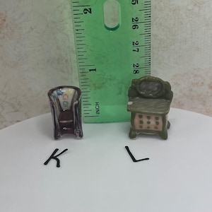 May include: Miniature ceramic furniture set, including a chair and a dresser. The chair is dark with a patterned back, and the dresser is green with pink drawer accents. A ruler is in the background.