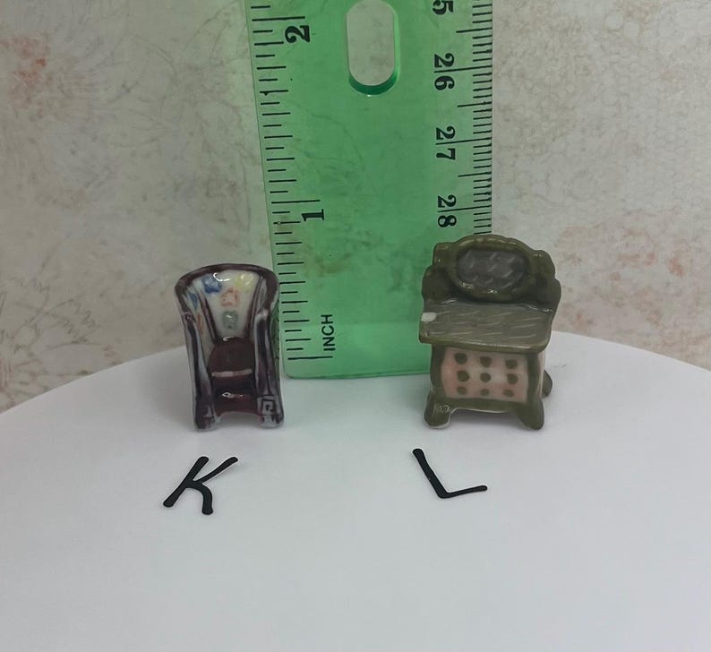May include: Miniature ceramic furniture set, including a chair and a dresser. The chair is dark with a patterned back, and the dresser is green with pink drawer accents. A ruler is in the background.