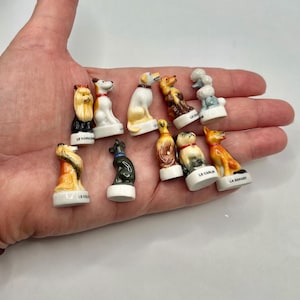 May include: A collection of small, ceramic dog figurines in various breeds, including a poodle, a Yorkshire terrier, and a beagle. Each figurine is painted with detailed features and rests on a small, white base. The figurines are held in a hand.