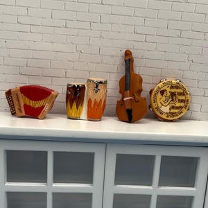 May include: A collection of miniature musical instruments, including an accordion, drums, a violin, and a tambourine. The accordion is red and gold, the drums are brown and orange, the violin is brown, and the tambourine has a beige face with text.